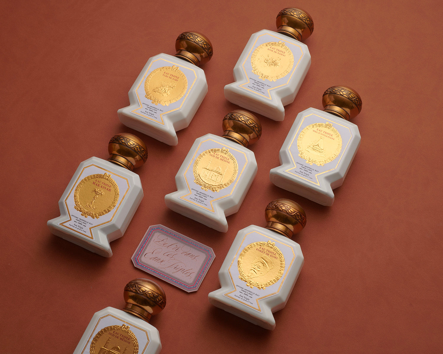 Officine Universelle Buly Eau Triple water-based perfume bottles arranged on terracotta with a calligraphy card